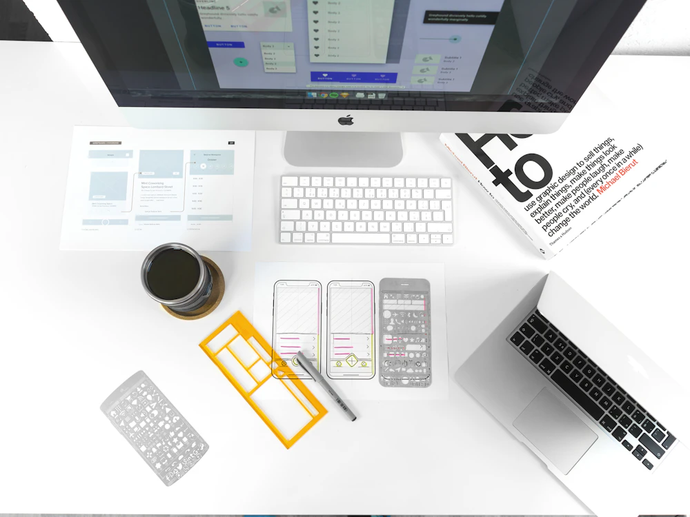 Design workstation with interface sketches, a laptop, and a desktop monitor